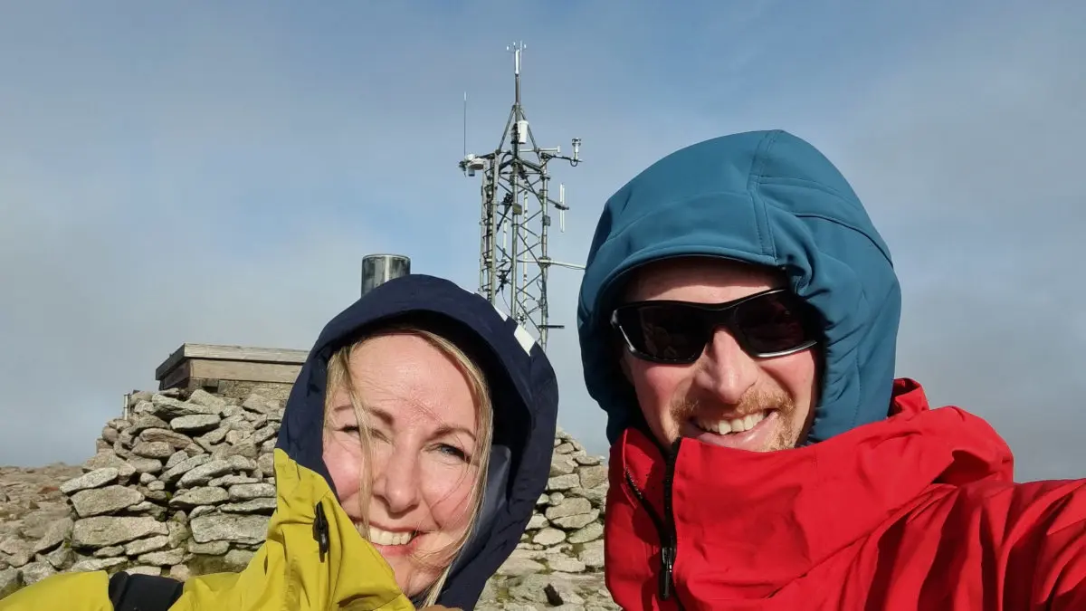 Two hikers in the wind on Cairn Gorm mountain summit in Scotland